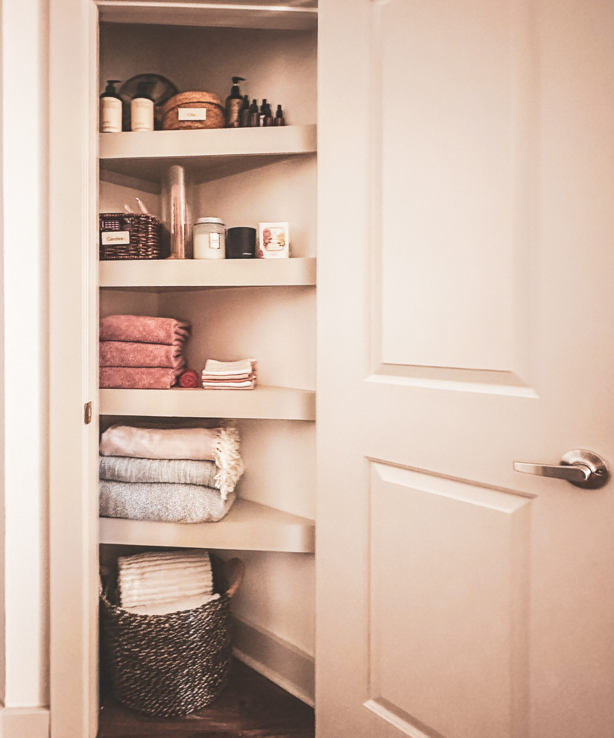 A hall closet with neatly folded towels, woven baskets, and simple storage bins on beige shelves — a real, lived-in example of home organization that reflects why organizing systems fail and how mindful design creates lasting calm.